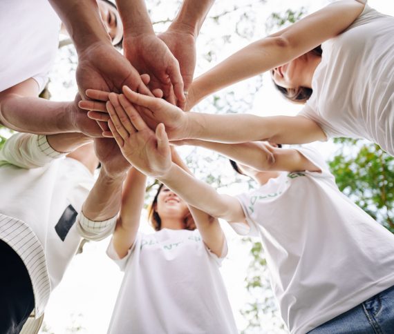 Team of student volunteers stacking hands to show support and unity before starting cleaning college campus